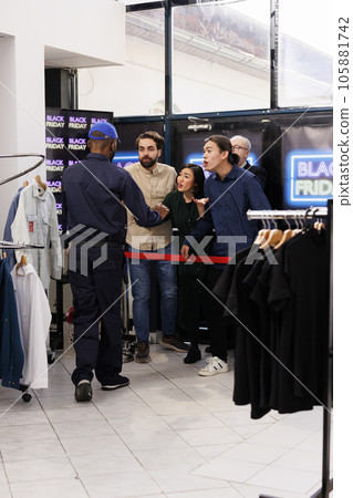 Eager emotional shoppers lined up outside of department store quarreling with clothing store security guard patrolling entrance, angry people tired of waiting for Black Friday deals in long line 105881742