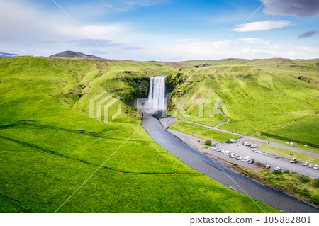 Skogafoss waterfall flowing from cliff surrounded by lush landscape in summer 105882801