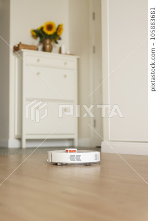 Modern wireless autonomous robotic vacuum cleaner washes wooden floor at light living room. Smart cleaning technology. Self-propelled white cleaning robot. Household appliances with remote control 105883681