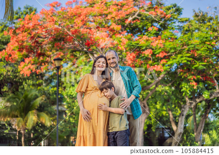 A loving family enjoying a leisurely walk in the park - a radiant pregnant woman after 40, embraced by her husband, and accompanied by their adult teenage son, savoring precious moments together 105884415