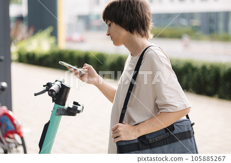 Teenage boy scan QR code on rent electric scooter to use him. Boy hurry to college Teenage boy scan QR code on rent electric scooter to use him. Boy hurry to college 105885267