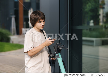 Teenage boy scan QR code on rent electric scooter to use him. Boy hurry to college Teenage boy scan QR code on rent electric scooter to use him. Boy hurry to college 105885272
