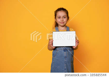 Adorable child girl showing digital tablet with white empty blank screen, smiling looking at camera, isolated background 105885544