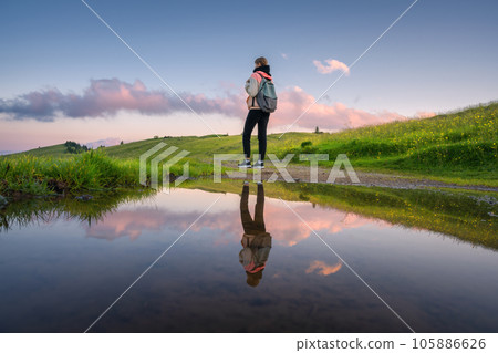 Woman with backpack reflected in lake at sunset in summer Woman with backpack reflected in lake at sunset in summer 105886626