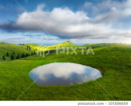 Aerial view of pond and green alpine meadows and hills at sunset Aerial view of pond and green alpine meadows and hills at sunset 105886689