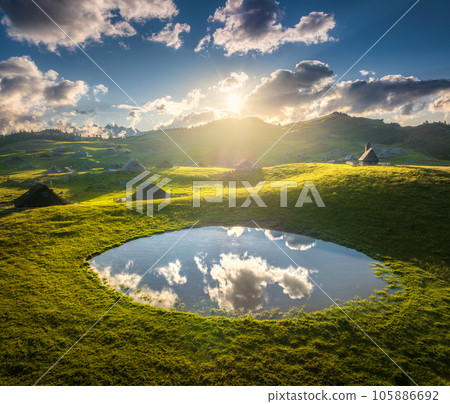 Aerial view of old mountain village, green hills, pond at sunset 105886692