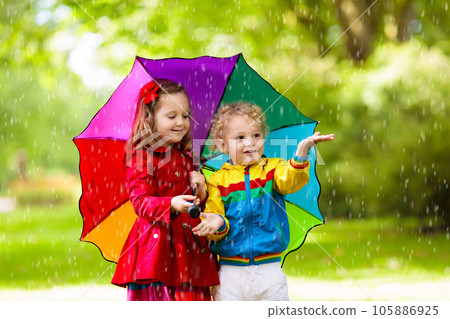 Kids playing in the rain under colorful umbrella Kids playing in the rain under colorful umbrella 105886925