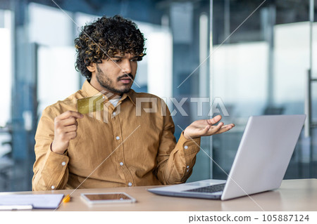 Upset and thinking businessman inside office, hispanic received rejection and error of online bank transfer, fraudulent actions, man holding bank credit card cheated. Upset and thinking businessman inside office, hispanic received rejection and error of online bank transfer, fraudulent actions, man holding bank credit card cheated. 105887124