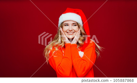 a cute beautiful woman in a Santa Claus hat on a red background. a cute beautiful woman in a Santa Claus hat on a red background. 105887868
