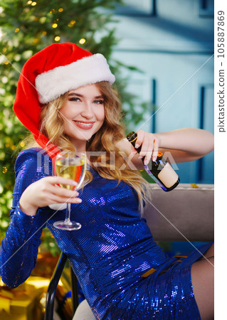 happy woman in santa's hat with bottle and glass of champagne by Christmas tree happy woman in santa's hat with bottle and glass of champagne by Christmas tree 105887869