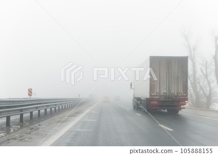 Driver POV on traffic on blue foggy misty rainy slush highway intercity road with low poor visibility on cold winter autumn morning. Seasonal bad rainy weather accident danger warning. car fog light 105888155