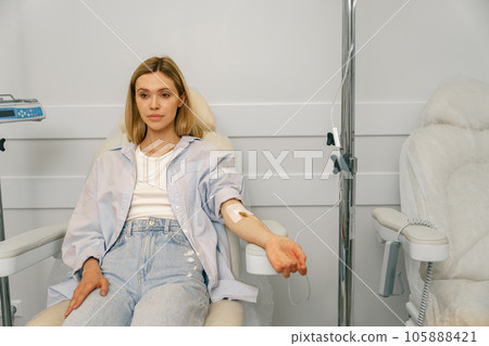 Attractive woman sitting in armchair while receiving IV infusion during treatment in hospital 105888421