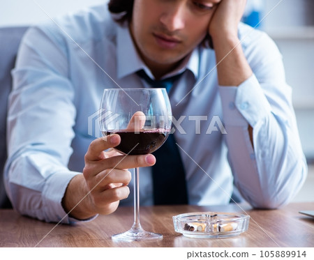 Male employee drinking alcohol and smoking cigarettes at workpla Male employee drinking alcohol and smoking cigarettes at workpla 105889914
