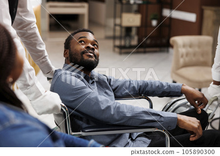 Happy young African American man using wheelchair during travel, receiving help and assistance in wheelchair-friendly and accessible hotel. People with mobility impairment and traveling 105890300