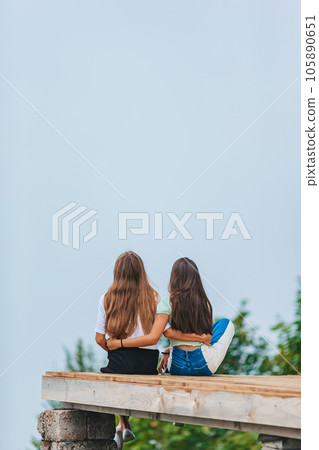 Back view of young girls sit on a terrace at a height in the mountains against the backdrop of fog and mountains 105890651