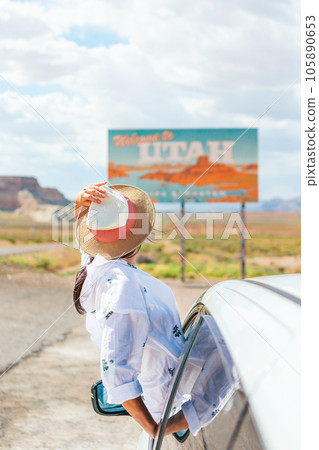 Beautiful woman on her trip by the car. Welcome to Utah road sign. Large welcome sign greets travels in Monument Valley, Utah 105890653