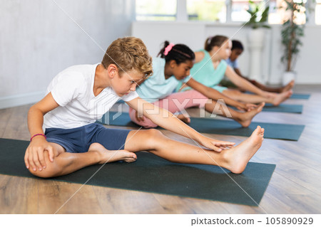 Kids practicing yoga, doing Head to Knee Forward Bend exercise, Janu Sirsasana pose, working out in yoga studio. Kids practicing yoga, doing Head to Knee Forward Bend exercise, Janu Sirsasana pose, working out in yoga studio. 105890929