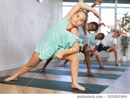 In sport studio with group of friends, girl perform elongated lateral angle, Parshvakonasana. In sport studio with group of friends, girl perform elongated lateral angle, Parshvakonasana. 105891064