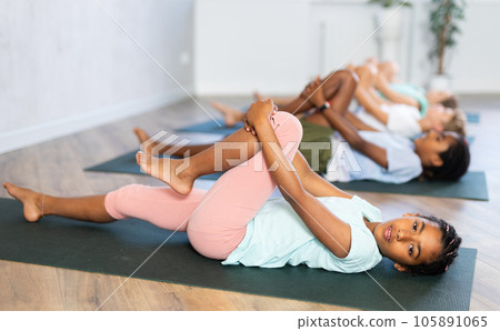 At yoga class African girl is lying on back, bent one leg at knee and raised it to chest At yoga class African girl is lying on back, bent one leg at knee and raised it to chest 105891065