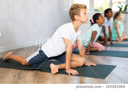 Children practicing yoga positions during group training in fitness center, performing stretching asana Urdhva Shvanasana Children practicing yoga positions during group training in fitness center, performing stretching asana Urdhva Shvanasana 105891069