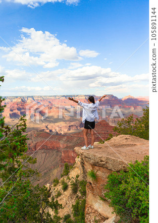 Happy young woman on a steep cliff taking in the amazing view over famous Grand Canyon at sunset, Grand Canyon National Park, Arizona, USA 105891144