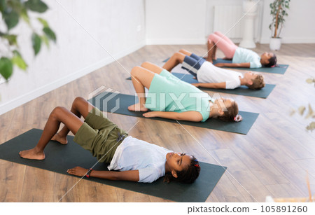 In sport studio with group of friends, African boy perform bridge pose, setu bandha sarvangasana In sport studio with group of friends, African boy perform bridge pose, setu bandha sarvangasana 105891260