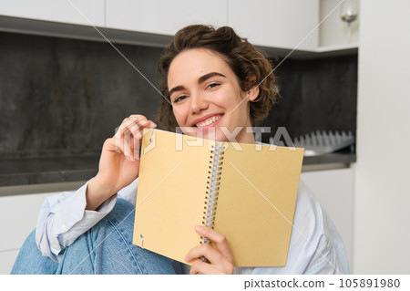 Image of brunette girl at home, holding notebook, reading through her notes, preparing for exam, doing homework in kitchen 105891980