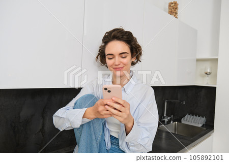 Portrait of woman sitting at home with mobile phone, online shopping on smartphone app, spending time indoors 105892101