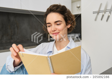 Image of brunette girl reading through her notes, writing in journal, studying while sitting at home 105892166