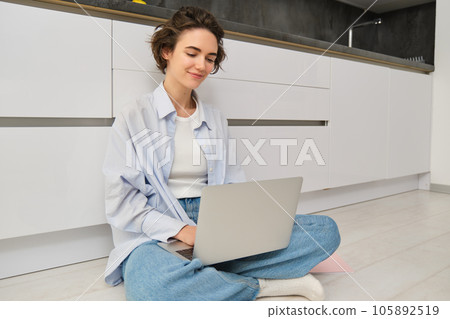 Young woman studying on floor. Girl with laptop works from home, types on computer, smiles and feels creative Young woman studying on floor. Girl with laptop works from home, types on computer, smiles and feels creative 105892519