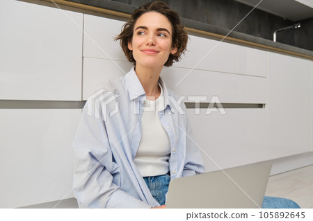 Young woman studying on floor. Girl with laptop works from home, types on computer, smiles and feels creative Young woman studying on floor. Girl with laptop works from home, types on computer, smiles and feels creative 105892645