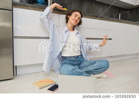 Happy young woman stretches her arms, sits on floor with laptop, finishes her remote work, completes homework on computer Happy young woman stretches her arms, sits on floor with laptop, finishes her remote work, completes homework on computer 105892650