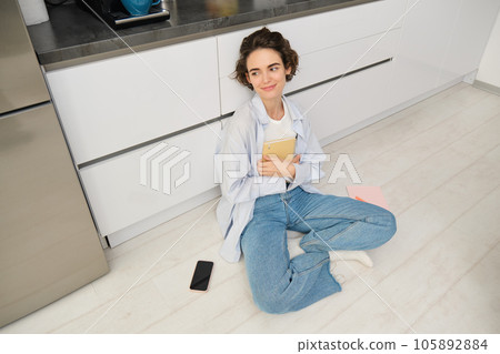Upper angle shot of young woman sitting on kitchen floor, revising for exam, reading her notes, doing homework at home Upper angle shot of young woman sitting on kitchen floor, revising for exam, reading her notes, doing homework at home 105892884