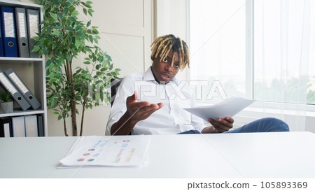 Report meeting. Work discussion. Video chat. Tensed business man sitting at office desk speaking about project documents gesticulating at modern workplace. Report meeting. Work discussion. Video chat. Tensed business man sitting at office desk speaking about project documents gesticulating at modern workplace. 105893369