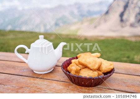 Teapot with tea and delicious National Kazakh pastries baursak. Street cafe in the highlands with a view of the mountains.. Fry dough in boiling oil in a frying pan. 105894746