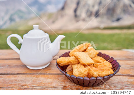 Teapot with tea and delicious National Kazakh pastries baursak. Street cafe in the highlands with a view of the mountains.. Fry dough in boiling oil in a frying pan. Teapot with tea and delicious National Kazakh pastries baursak. Street cafe in the highlands with a view of the mountains.. Fry dough in boiling oil in a frying pan. 105894747