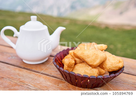 Teapot with tea and delicious National Kazakh pastries baursak. Street cafe in the highlands with a view of the mountains.. Fry dough in boiling oil in a frying pan. 105894769