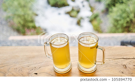 Two cups of ginger root tea with lemon, honey and mint on a wooden table and High-mountain river in the background. Walk in the mountains and relax in a cozy cafe. Hiking on a day off 105894770