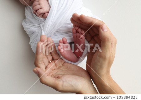 The palms of the father, the mother are holding the foot of the newborn baby. Feet of the newborn on the palms of the parents. Photography of a child's toes, heels and feet. Black and white macro. 105894823