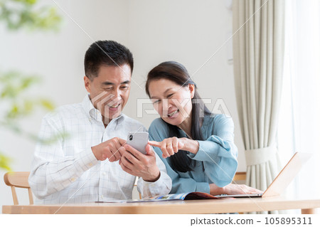 Senior couple looking at a travel brochure and making a reservation 105895311