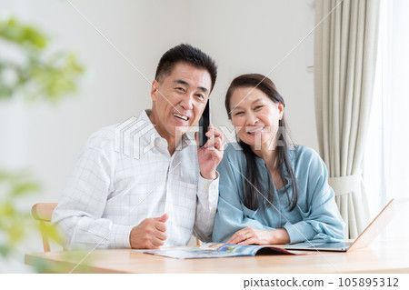 Senior couple looking at a travel brochure and making a reservation Senior couple looking at a travel brochure and making a reservation 105895312