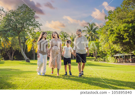 A loving family enjoying a leisurely walk in the park - a radiant pregnant woman after 40, embraced by her husband, and accompanied by their adult teenage children, savoring precious moments together 105895840