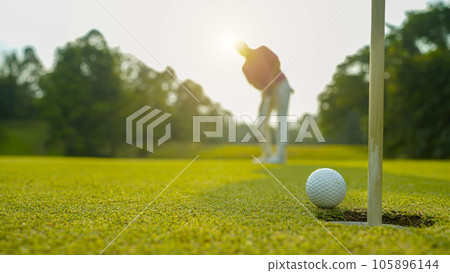 Golfer putting ball on the green golf, lens flare on sun set evening time. 105896144