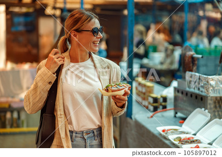 Stylish mature woman is having a takeaway fast food lunch on food market and looking at side 105897012