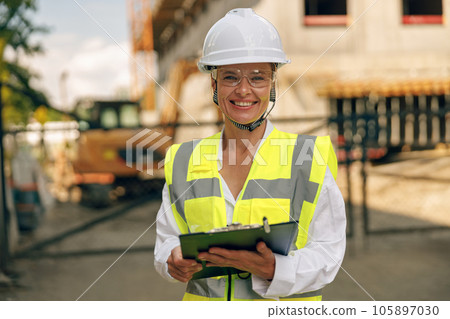 Female engineer in protective helmet making notes on construction site and looking at camera 105897030