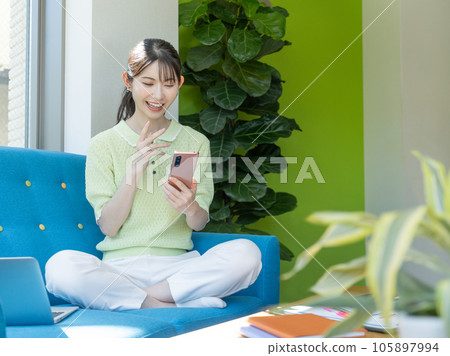 坐在沙發上用智能手機進行視頻通話的年輕女子 坐在沙發上用智能手機進行視頻通話的年輕女子 105897994