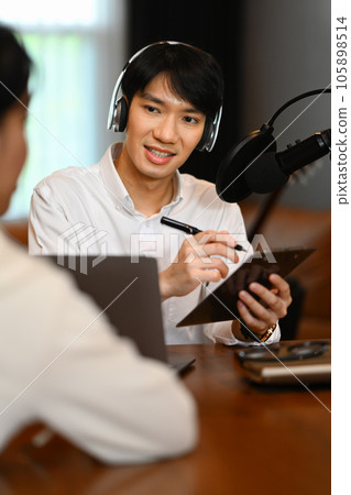 Male radio host discussing various topics with her guest while streaming live audio podcast from home studio Male radio host discussing various topics with her guest while streaming live audio podcast from home studio 105898514