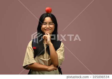 Smiling teenage asian girl with apple on head isolated on pink background. Health, nutrition and dieting 105898534