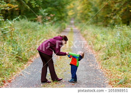 Little boy with his young mother in the autumn orest. Active family time on nature. Fun with little kids in fall days. Mum and toddler son walking in forest. 105898951
