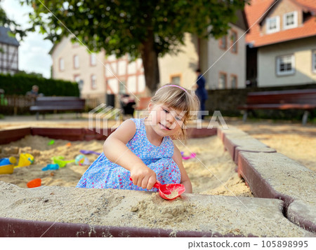 Adorable little girl on playground in sandpit. Toddler playing with sand molds and making mudpies. Outdoor creative activities for kids. 105898995